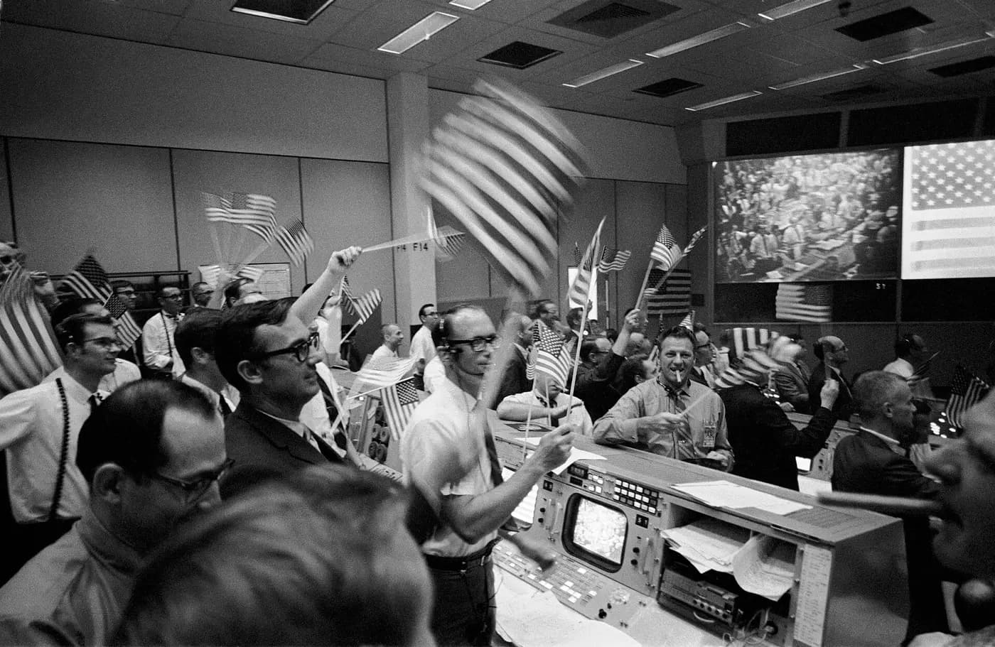 Flight controllers wave flags at their consoles in Houston's Mission Control as Apollo 11 returns, July 1969