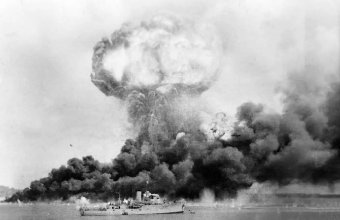 The Neptuna exploding and oil-tank smoke rising over Darwin harbour during the first Japanese air raid, 19 February 1942